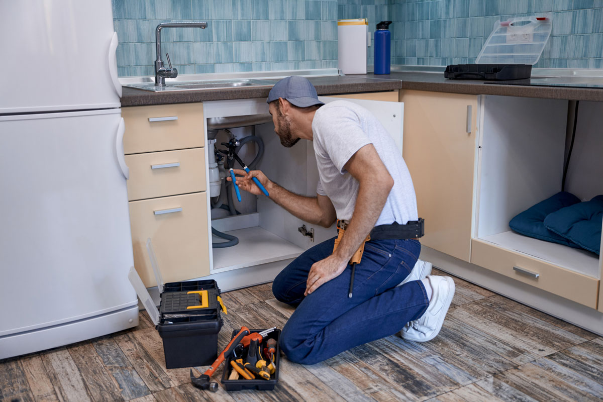 Young caucasian male worker fixing tubes under kitchen sink stock photo